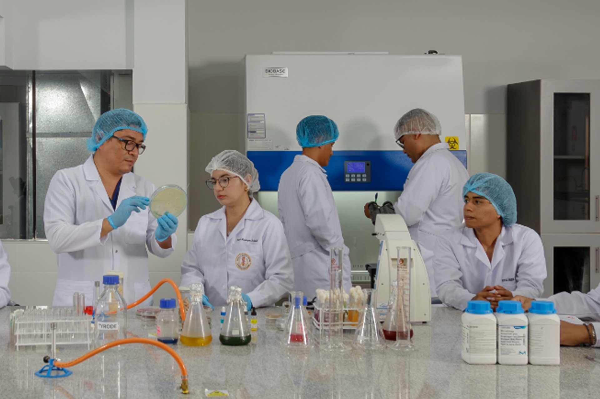 Estudiantes de la USS en un laboratorio, con un docente mostrando una placa de cultivo